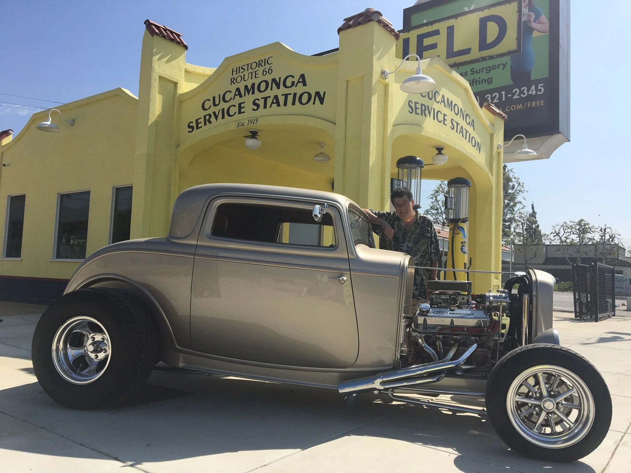 A visitor with a classic hot rod in front of the fully restored, brightly painted station